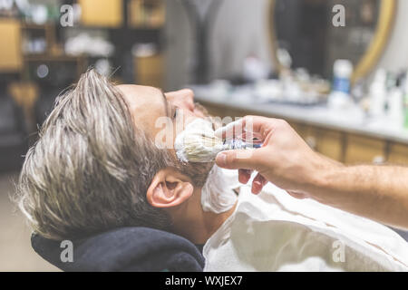 Parrucchiere professionale applicazione di schiuma da barba sulla pelle del client in barberia. Foto Stock