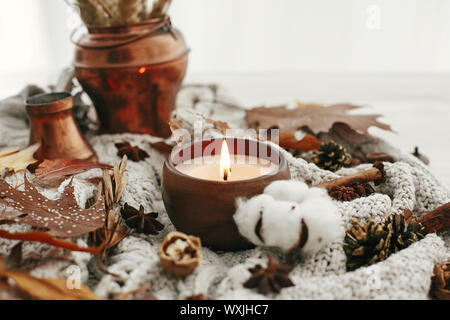 Ciao autunno, accogliente immagine ispiratrice.Hygge lifestyle. Candela con bacche e foglie di autunno, anice, erbe, ghiande, dadi , Cannella, cotone su bianco knitte Foto Stock