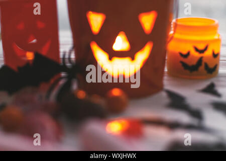 Immagine sfocata di incandescente jack o lantern faccia festosa, candy, teschi, nero pipistrelli, fantasma, spider decorazioni in legno bianco in sfondo scuro. Felice H Foto Stock