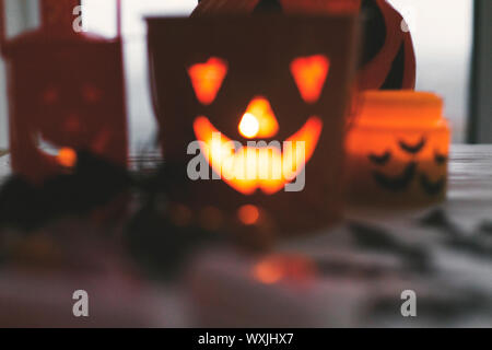 Immagine sfocata di incandescente jack o lantern faccia festosa, candy, teschi, nero pipistrelli, fantasma, spider decorazioni in legno bianco in sfondo scuro. Felice H Foto Stock