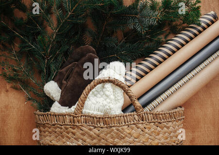 Cesto rustico con rami di abete,festosa carta di avvolgimento, intimo guanti e hat su legno rustico sfondo. Lay piatto. Vacanze invernali preparati. L lento Foto Stock