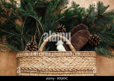 Cesto rustico con rami di abete, intimo guanti, coni in legno rustico sfondo. Lay piatto. Vacanze invernali preparati. I migliori auguri di Buon Natale Foto Stock