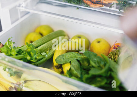 Plastica banane libero,insalata di spinaci, sedano, mele, arancione in frigo. Rifiuti Zero a fare la spesa. Ortaggi freschi nel cassetto aperto in frigorifero. Foto Stock