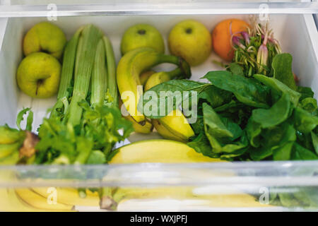 Plastica banane libero,insalata di spinaci, sedano, mele, arancione in frigo. Rifiuti Zero a fare la spesa. Ortaggi freschi nel cassetto aperto in frigorifero. Foto Stock