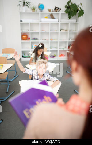 Scolaro alzando la mano mentre avente risposta per insegnante Foto Stock