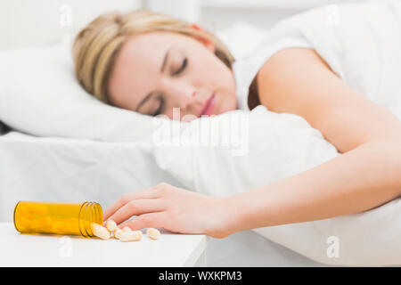 Giovane donna che dorme nel letto con focus sulla fuoriuscita di bottiglia di pillole a casa Foto Stock