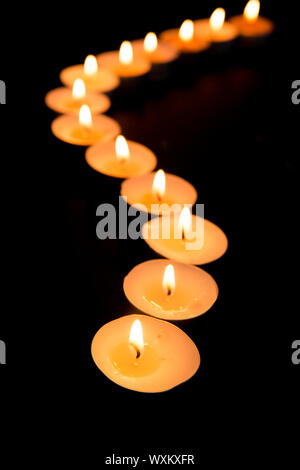 Tealight candele illuminazione in una linea curva nel buio Foto Stock