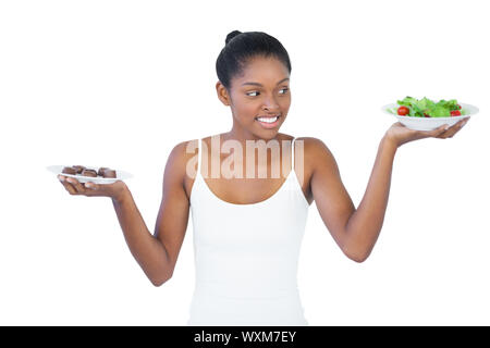 Allegra donna di decidere di mangiare in modo sano o non è su sfondo bianco Foto Stock