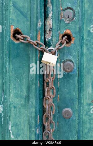 Serrature e un lucchetto e la catena su una vecchia casa porta con peeling paint Foto Stock