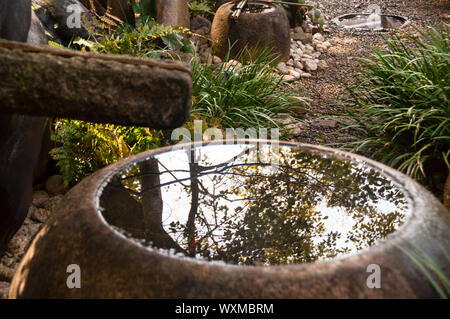 Riflessi in un bacino di pietra da una fontana di bambù giapponese in una cantina di sake a Osaka, in Giappone. Foto Stock