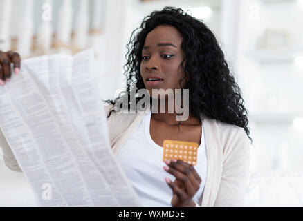 Scioccato americano africano donna leggere il foglietto prima di prendere le pillole contraccettive Foto Stock