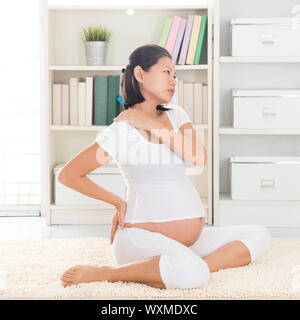 Spalla o dolore al collo. Otto mesi di gravidanza donna asiatica tenendo la schiena e la spalla mentre è seduto su un pavimento a casa. Foto Stock