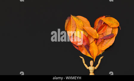 Manichino di legno azienda grande cuore di foglie secche su nero Foto Stock