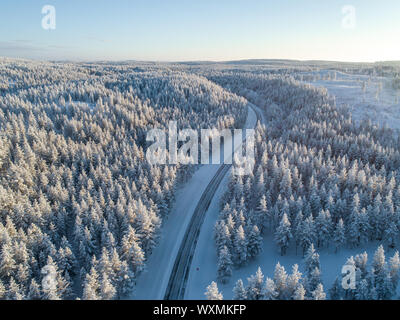Curva road nel mezzo di una fitta foresta a giornata invernale in Lapponia, Finlandia Foto Stock