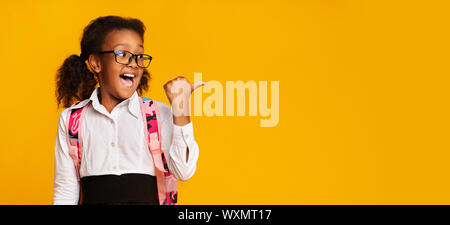 Eccitato nero di puntamento Schoolgirl Thumbs a copiare lo spazio in Studio Foto Stock