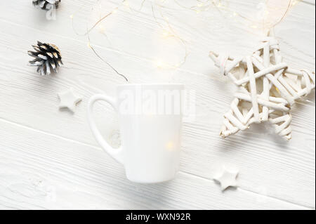 White tazza da caffè con coni di Natale e stelle. Spazio per il testo o il design. Mockup tazza bianca su un bianco sullo sfondo di legno. Piatto, laici top view foto Foto Stock