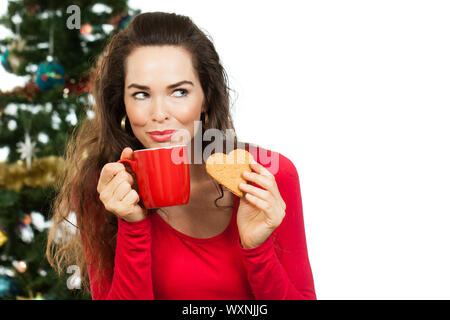 Bella donna gustando una bevanda calda e gingerbread cookie nella parte anteriore di un albero di Natale. Isolato su bianco. Foto Stock