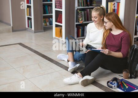 Due amiche seduto sul pavimento in libreria, studiare con il computer portatile Foto Stock