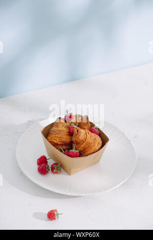 Croissant con lamponi. I lamponi con croissant. Croissant su uno sfondo luminoso con bacche di lampone Foto Stock