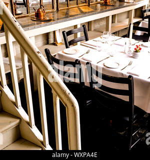 Tabella tradizionale impostazione in un Ristorante Sala da pranzo con sedie in legno, piatti e bicchieri di vino Foto Stock