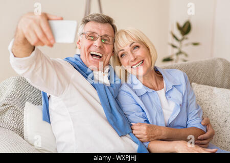 Nonni moderni tenendo selfie sul cellulare, appoggiata sul divano Foto Stock