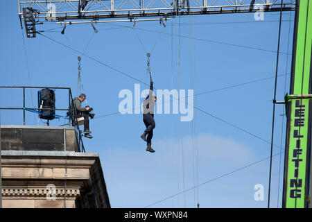 Tetti, West College Street, Edimburgo, Scozia, Regno Unito. Xvii Settembre 2019. Tempo chiaro di sole e cielo blu per le riprese di "Fast e Furious 9', nella foto, film cameraman e attore stunt sospesa a mezz aria da un gantry che essi zip puleggia di filo su mentre è attaccata a una massiccia gru, come questa scena continua per un secondo giorno al di sopra del centro della città strade. Foto Stock