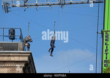 Tetti, West College Street, Edimburgo, Scozia, Regno Unito. Xvii Settembre 2019. Tempo chiaro di sole e cielo blu per le riprese di "Fast e Furious 9', nella foto, film cameraman e attore stunt sospesa a mezz aria da un gantry che essi zip puleggia di filo su mentre è attaccata a una massiccia gru, come questa scena continua per un secondo giorno al di sopra del centro della città strade. Foto Stock