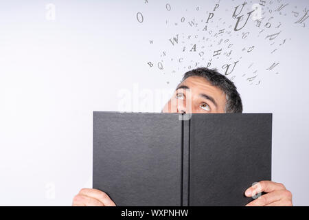 Uomo in possesso di un notebook con stupore sul suo volto osservando alcune lettere in aria su uno sfondo bianco. Il concetto di istruzione Foto Stock