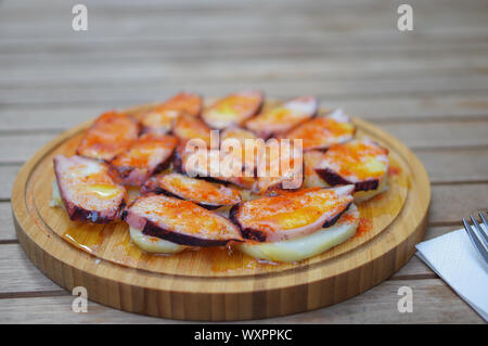 Fette di polpo grigliate con pimento paprika in polvere e patate a fette su un piatto di legno rotondo Foto Stock