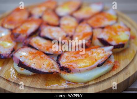 Fette di polpo grigliate con pimento paprika in polvere e patate a fette su un piatto di legno rotondo Foto Stock