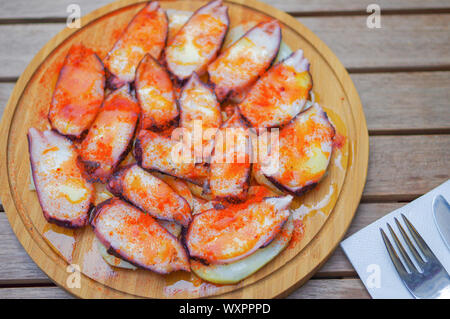 Fette di polpo grigliate con pimento paprika in polvere e patate a fette su un piatto di legno rotondo Foto Stock