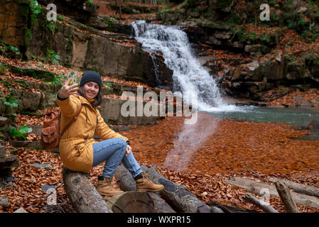 Donna seduta sul log guardando a cascata la stagione autunnale Foto Stock