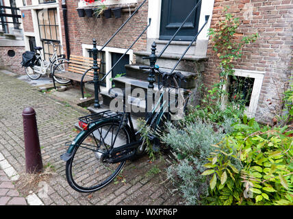 Tipico di Amsterdam scena Canal-Side con biciclette parcheggiate accanto all'ingresso a case Foto Stock