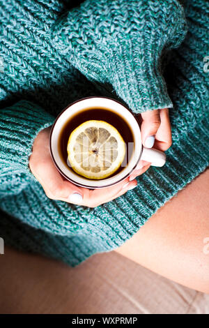 Mani femminili tenendo la tazza di tè caldo con limone in mattina. Giovane donna rilassante tazza di tè a portata di mano. Buon tè del mattino o avere un giorno felice concetto del messaggio. Foto Stock