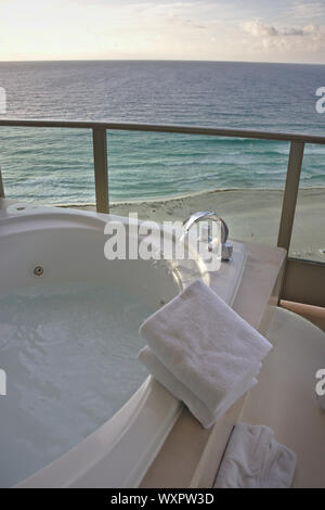 Svuotare una vasca idromassaggio con acqua e asciugamani bianchi di fronte ad una spiaggia di sabbia con un blu oceano Foto Stock