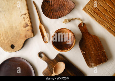 Vari articoli per la tavola in legno. I taglieri, cucchiai di diverse forme, piastra e ciotola sulla tovaglia di lino Foto Stock