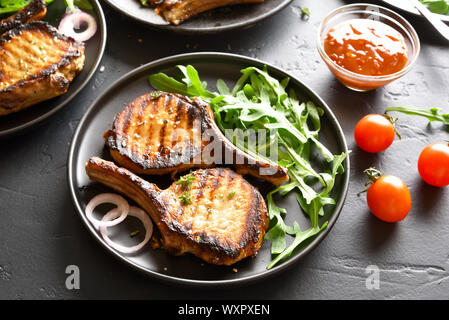 Grigliata di bistecche di maiale con verdure sulla piastra nera. Foto Stock