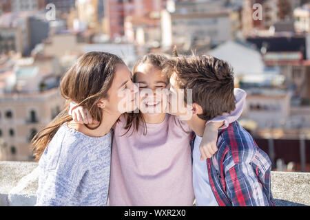 Dos hermanos besando a la vez un su hermana pequeña en la azotea Foto Stock