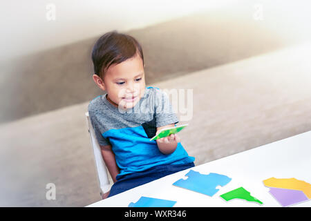 Una smart 3 anno vecchio ragazzo tenendo un pezzo di puzzle in mano e cercando di assemblare un North American mappa puzzle. Foto Stock