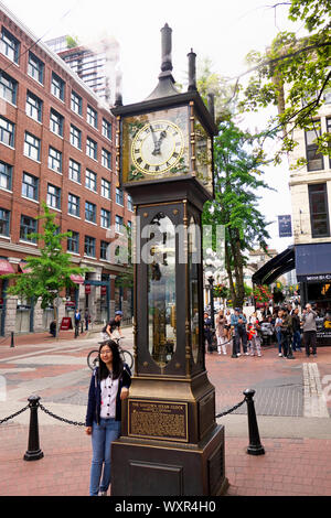 Una giovane donna asiatica si appoggia contro il Gastown Steam Clock, Vancouver, B. C., Canada Foto Stock