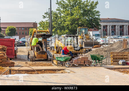 HICKORY, NC, Stati Uniti d'America-13 Settembre 2019: costruzione di scena, con autista salendo sul caricatore frontale e lavoratore mattoni di impilaggio in una carriola Foto Stock