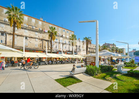 Pomeriggio estivo sul lungomare di Riva presso il porto di Spalato Croazia come turisti e un ciclista godere gli alberi di palme e caffetterie sulla costa Foto Stock