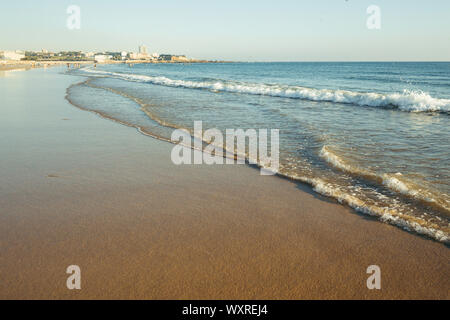 Litorale della spiaggia della città con onde al tramonto. Foto Stock