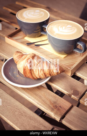 Due grandi tazze di cappuccino e croissant su una tabella in un street cafe. Colpo verticale Foto Stock