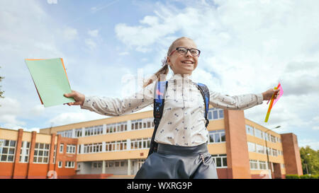 Felice undici anni di schoolgirl corre con uno zaino e quaderni dopo la scuola. Foto Stock