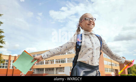 Felice undici anni di schoolgirl corre con uno zaino e quaderni dopo la scuola. Foto Stock