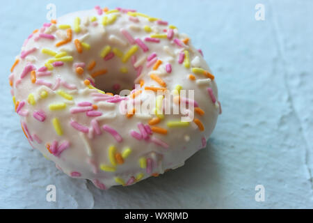 Ciambella in smalto bianco con multi-Spruzzi di colore blu su sfondo a trama close-up Foto Stock