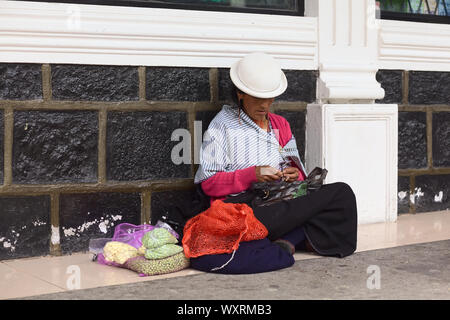 BANOS, ECUADOR - 25 FEBBRAIO 2014: Donna non identificata che spellano l'aglio e vende aglio e piselli sulla strada seduta sul marciapiede Foto Stock