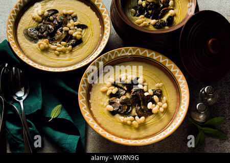 Zuppa di funghi italiana con fagioli cannellini e finocchi in pentole di creta su un tavolo. Autunno sano cibo vegan. top shot Foto Stock