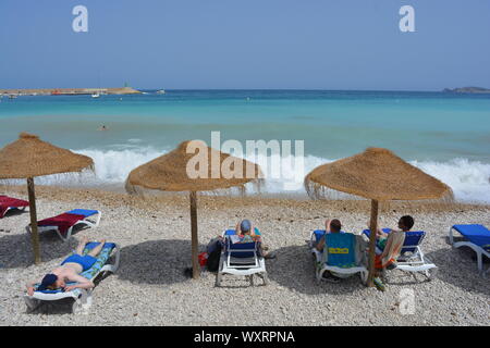 Estate spiaggia scena con uomo a prendere il sole su una sedia a sdraio, parasoli e persone su La Grava beach, Javea, Xabia sulla Costa Blanca, Spagna Foto Stock